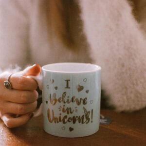 Hand holding a unicorn-themed mug with a cozy and warm vibe, perfect for morning coffee or tea.